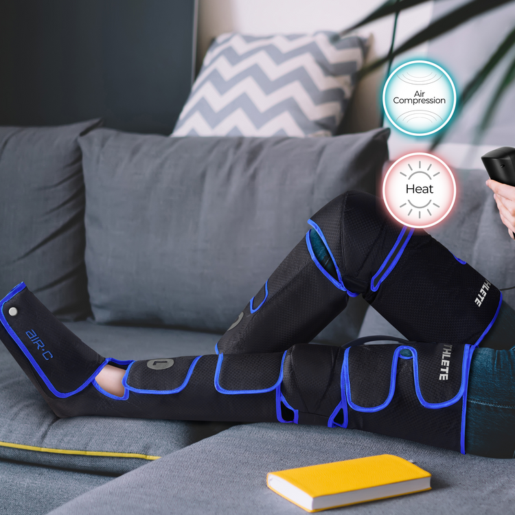 Person using air compression and heat therapy on legs with a gray couch and yellow book in the background.